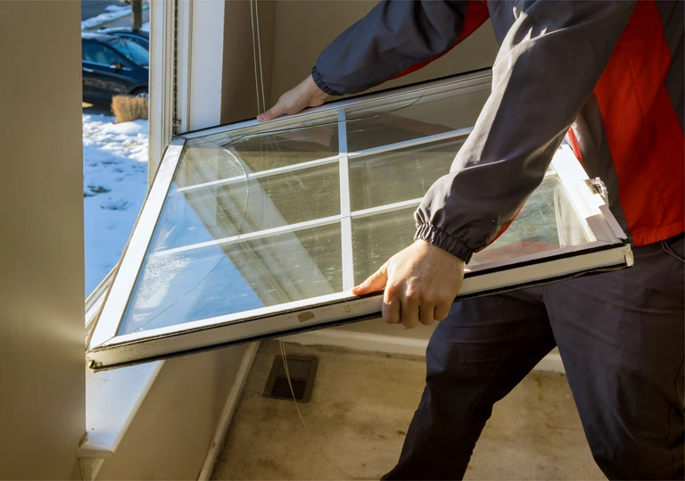 Mężczyzna wynosi z&nbsp;pomieszczenia zdemontowane, stare skrzydło okienne z&nbsp;poprzecznymi szprosami