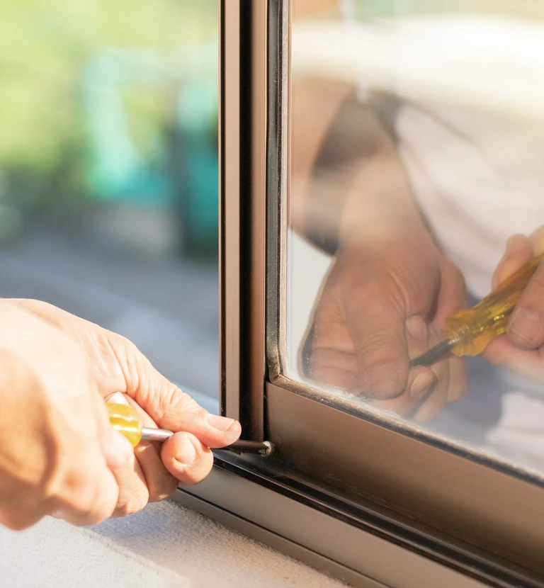 Serwisant używa śrubokrętu do&nbsp;regulacji dolnego zawiasu w&nbsp;oknie